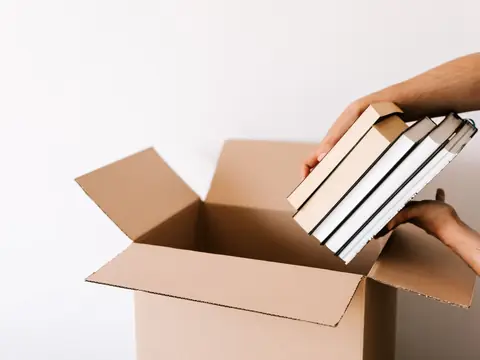 Hands placing books into an open cardboard box