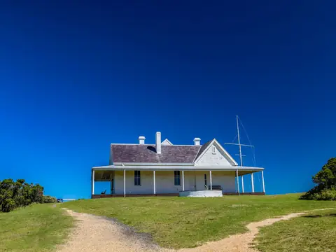 A white house with a long veranda on a grassy rise under a blue sky