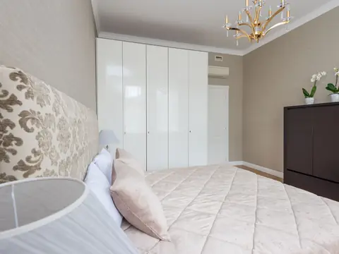 A bedroom with a tall built-in white wardrobe and a dark chest of drawers