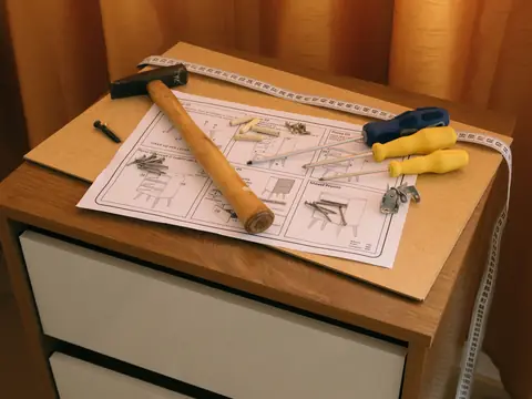 A hammer, screwdrivers, a tape measure and assembly instructions on a bedside cabinet