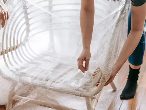 Hands wrapping a cane chair in bubble wrap