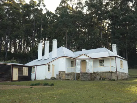 A white stone cottage with tall chimneys in front of tall gum trees