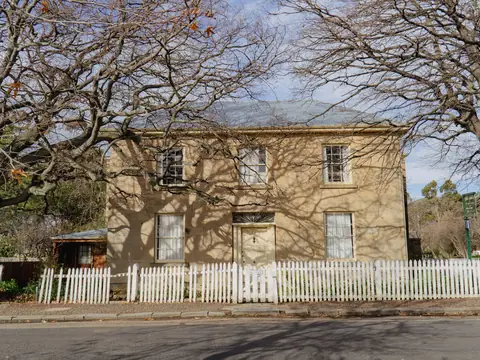 A two-storey sandstone house behind a white picket fence and bare trees