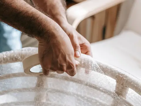 Hands steadying a cane chair while it is wrapped for a move