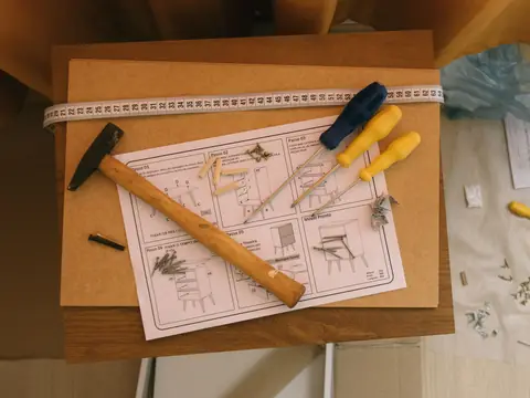 A tape measure, a hammer and screwdrivers on furniture assembly instructions, from above